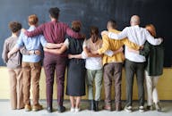 A diverse group of adults in casual outfits hugging in front of a chalkboard, symbolizing teamwork. leadership