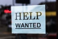 Close-up of a Help Wanted sign taped to a glass window in a storefront. 
