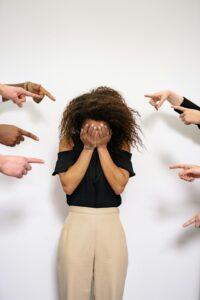A stressed woman covers her face as multiple hands point accusatorily in a studio setting. 