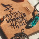 Brown booklet with inspiring text and necklace, featuring a blue crystal pendant in warm daylight.